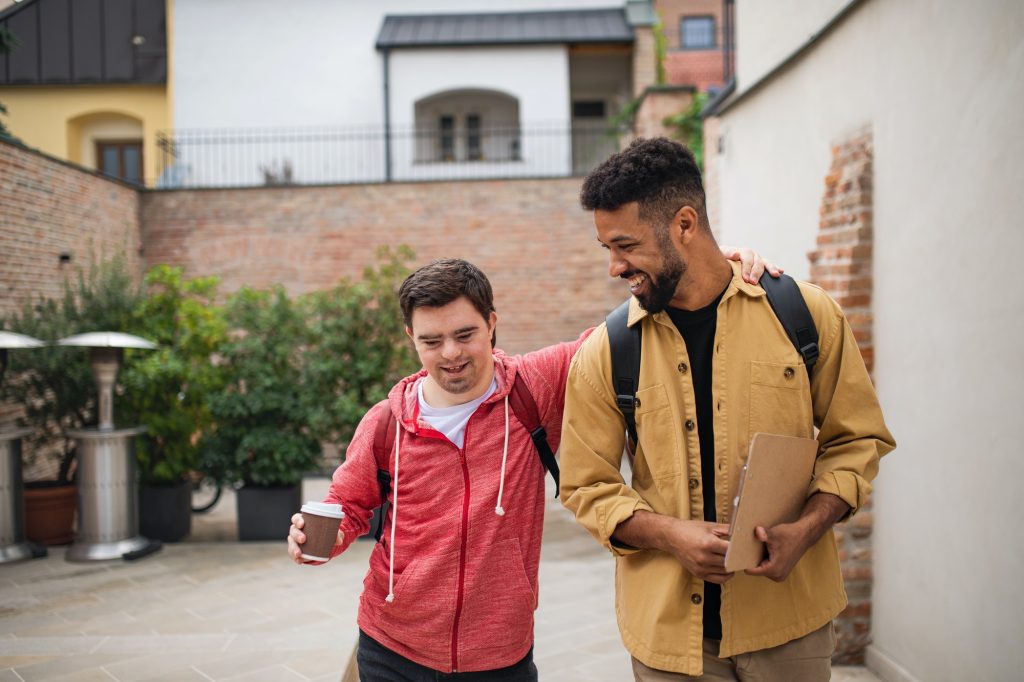 Young man with Down syndrome and his mentoring friend walking and talking outdoors